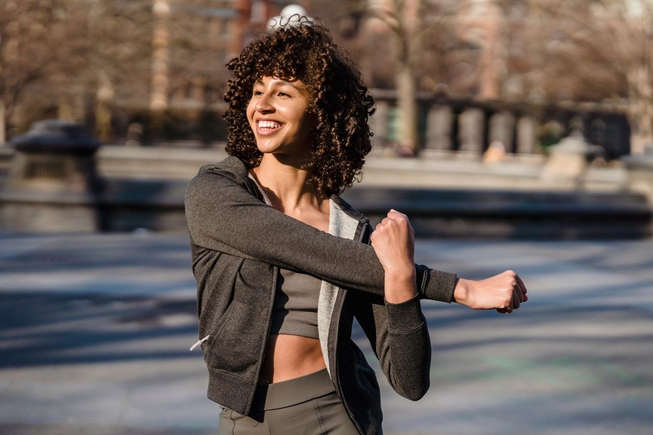 Content young ethnic female athlete in sportswear with curly hair working out while looking away on sunny street